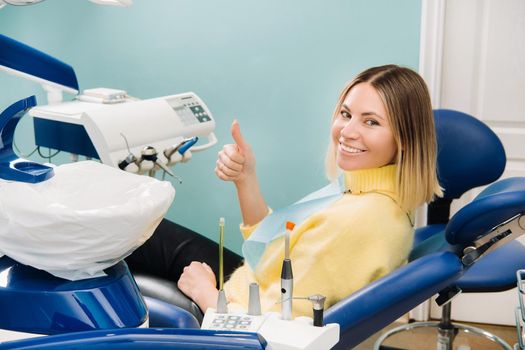 Beautiful girl patient shows the class with her hand while sitting in the Dentist's chair.