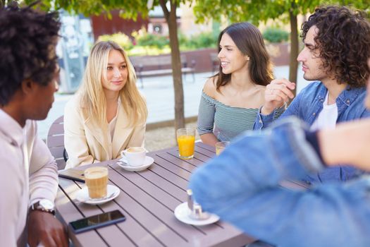 Multi-ethnic group of friends having a drink together in an outdoor bar. One of the men shows something on his smartphone to his friends.