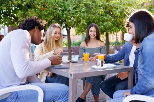 Multi-ethnic group of friends having a drink together in an outdoor bar. Young people having fun.