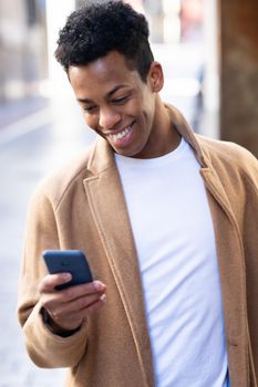 Young black man using his smartphone outdoors. Cuban guy smiling in urban background.