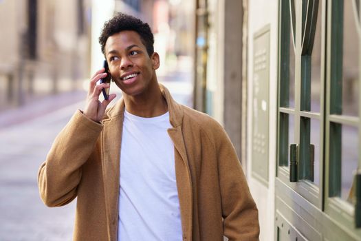 Young black man talking on the phone while walking down the street. Cuban guy smiling in urban background.