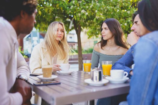 Multi-ethnic group of friends having a drink together in an outdoor bar. One of the men shows something on his smartphone to his friends.