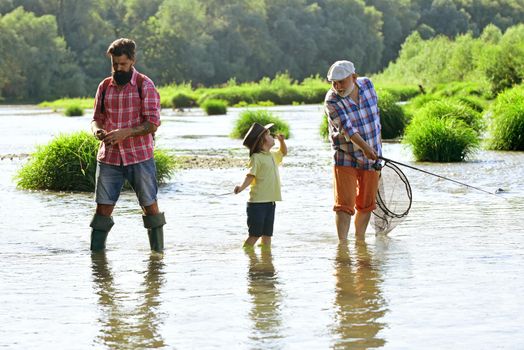 Happy grandfather, father and grandson with fishing rods on river berth. Fishing in river. Family bonding. Grandpa and grandson are fly fishing on river. Old and young