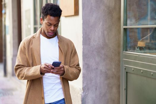 Young black man using his smartphone outdoors. Cuban guy smiling in urban background.