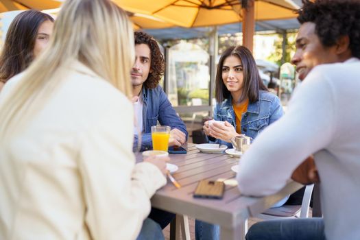 Multi-ethnic group of friends having a drink together in an outdoor bar. One of the men shows something on his smartphone to his friends.