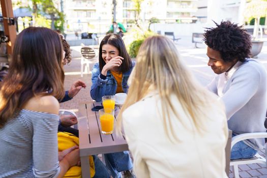 Multi-ethnic group of friends laughing and having a drink together in an outdoor bar.