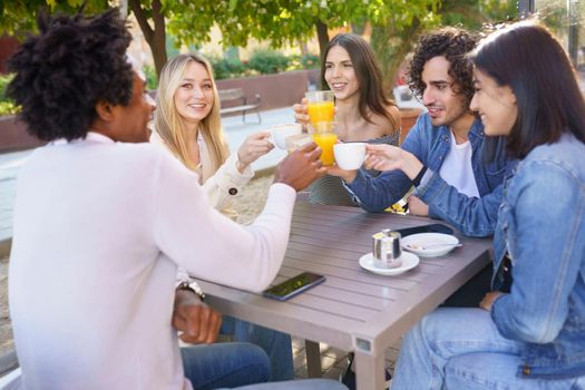 Multi-ethnic group of friends making a toast with their drinks while having a drink together at the outside table of a bar.