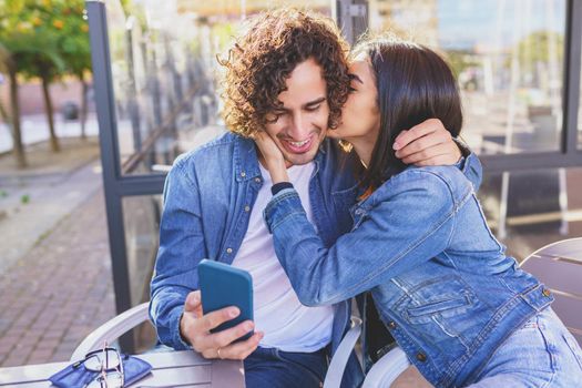 Arab couple looking at pictures taken with their smartphone, sitting on the terrace of a bar.