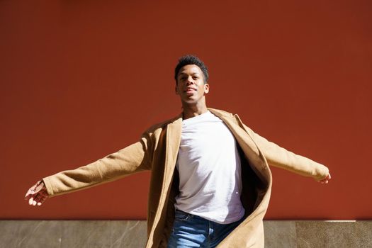 Young Cuban man dancing on red urban wall. Happy young black guy outdoors.