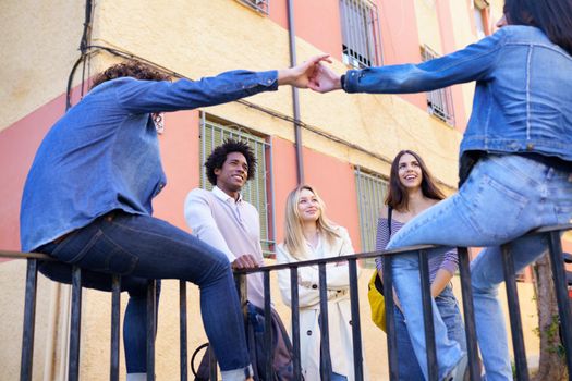 Multi-ethnic group of friends gathered in the street leaning on a railing. Young people having fun together.