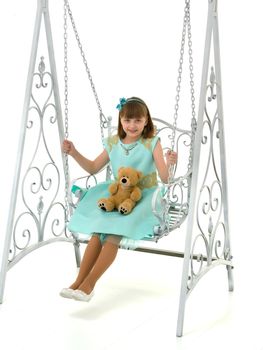 A little girl swings on a swing with a teddy bear. The concept of a happy childhood, the development of a child in the family. Isolated on white background.