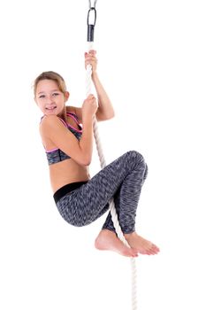 Smiling girl hanging on rope. Happy child wearing sports clothes exercising on rope against white background. Happy childhood, active lifestyle concept