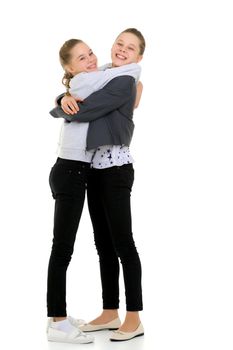 Lifestyle Portrait of Two Pretty Teen Girls Smiling, Hugging and Having Fun, Happy Beautiful Sisters in Fashionable Stylish Clothes Posing in Studio Against White Background