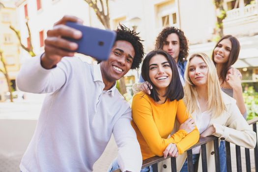 Multi-ethnic group of friends taking a selfie in the street with a smartphone. Young people having fun together.