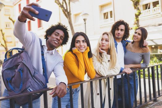 Black man with afro hair taking a smartphone selfie with his multi-ethnic group of friends outdoors.