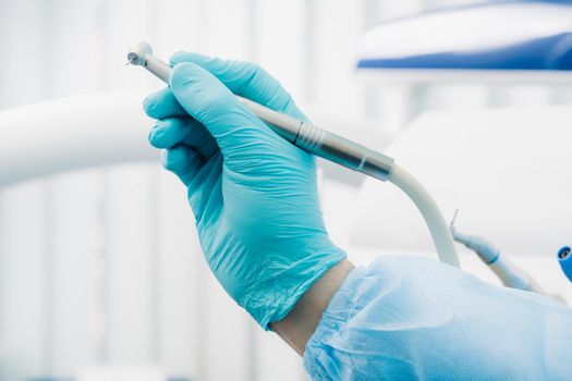 a dentist wearing gloves in the dental office holds a tool before working.