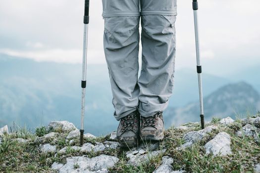 Hiker standing with trekking poles in the rocky mountains, front view of legs.