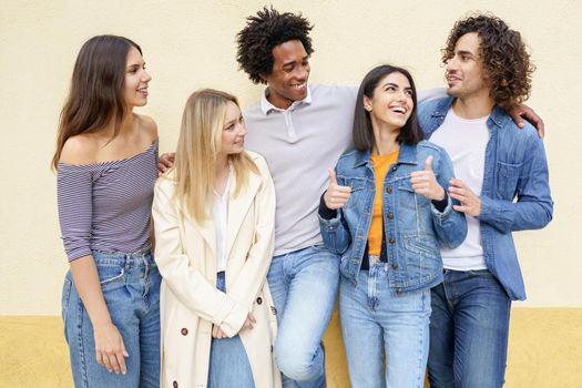 Multi-ethnic group of friends posing while having fun and laughing together against a yellow urban wall.