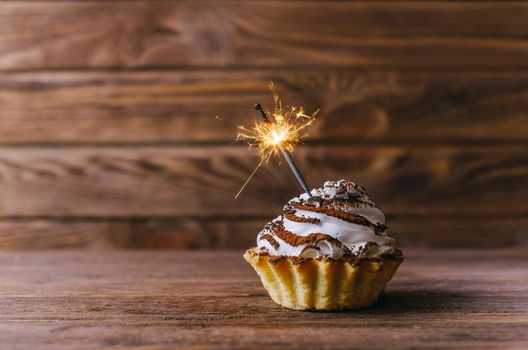 Holiday birthday cupcake with sparkler on a wooden background.