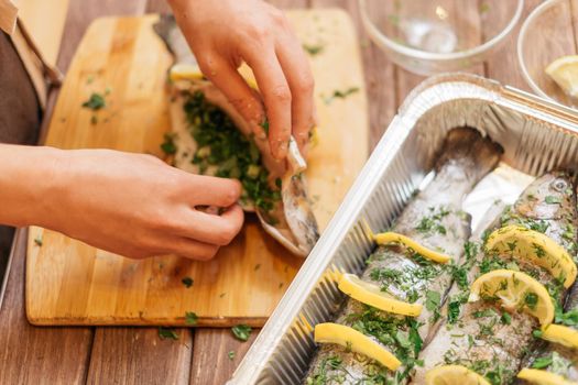 Female hands preparing fish trout with greenery on wooden board.