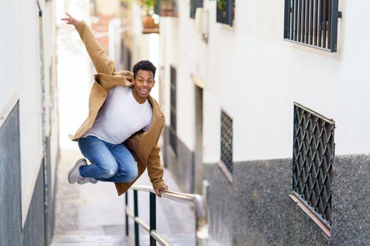 Young black man jumping for joy over a handrail in the street. Cuban guy.