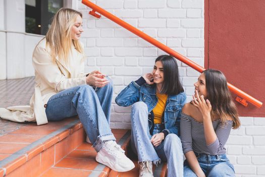 Multi-ethnic group of three female friends sitting on street steps talking.