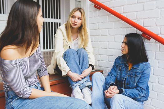 Multi-ethnic group of three female friends sitting on street steps talking.