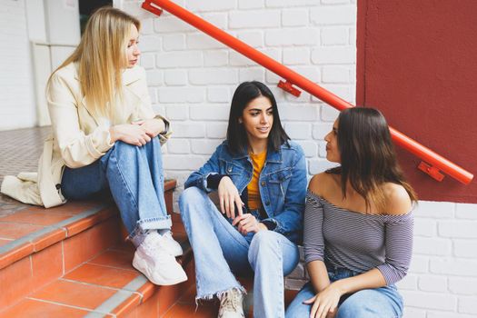 Multi-ethnic group of three female friends sitting on street steps talking.