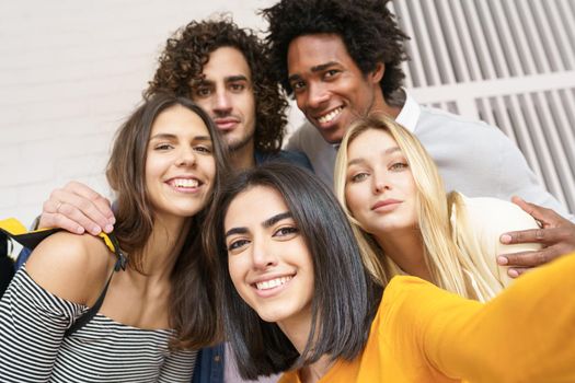 Multi-ethnic group of friends taking a selfie together while having fun in the street. Persian woman in the foreground.