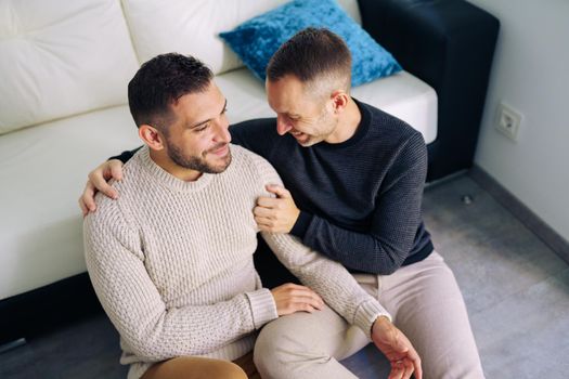 Gay couple sitting near the couch at home in a romantic moment. Homosexual relationship concept.