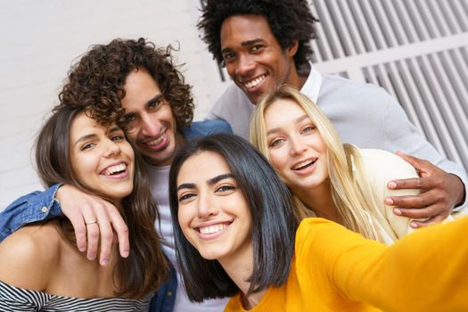 Multi-ethnic group of friends taking a selfie together while having fun in the street. Persian woman in the foreground.