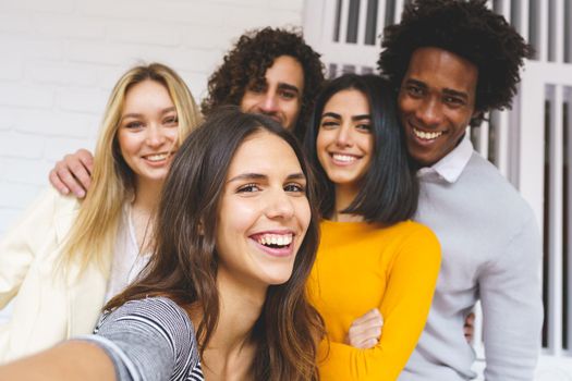 Multi-ethnic group of friends taking a selfie together while having fun in the street. Caucasian girl in the foreground.