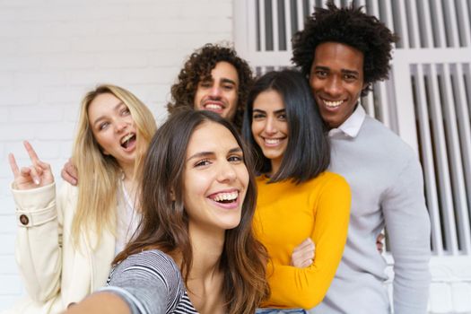 Multi-ethnic group of friends taking a selfie together while having fun in the street. Caucasian girl in the foreground.