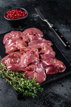 Raw chicken liver meat on marble board with thyme. Black background. Top view.