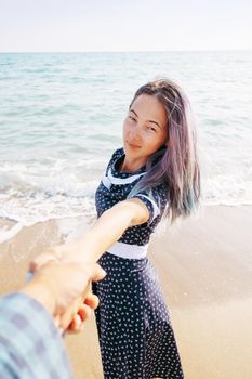 Couple in love resting on beach summer vacations. Beautiful young woman holding man's hand and leading him on sea, point of view shot.