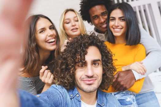 Multi-ethnic group of friends taking a selfie together while having fun in the street. Arab man with afro hair in the foreground.