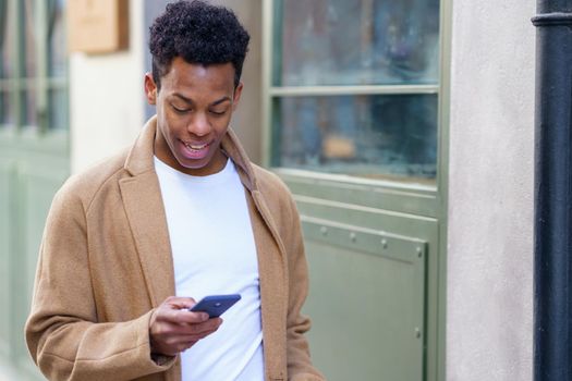 Young black man consulting his phone while walking down the street. Cuban guy in urban background.