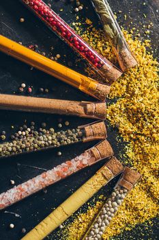 A set of spices in small jars with cork lids. Pink salt, ginger, turmeric, masala, paprika, smoked paprika. Spices on a black surface