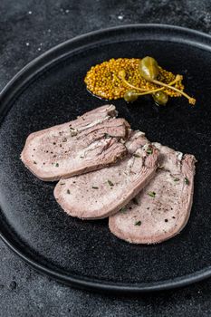 Pork boiled tongue slices on a plate. Black background. Top view.