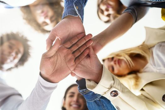 Multi-ethnic group of people putting their hands together. Friends with stack of hands showing unity and teamwork.