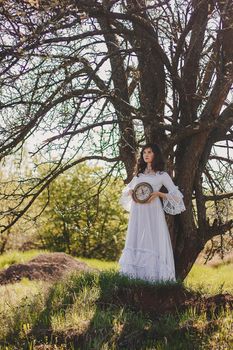 Portrait of carefree young woman in white vintage wedding style dress in spring cherry blossom garden valley.