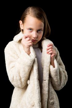 Pretty girl in fashionable outfit. Stylish beautiful girl wearing beige fur coat and jeans. Full length portrait of preteen child posing in studio against black background