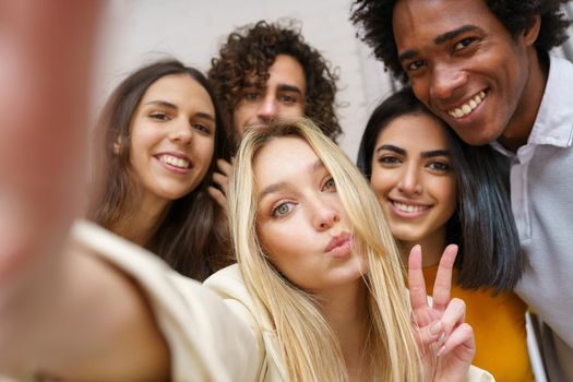 Multi-ethnic group of friends taking a selfie together while having fun in the street. Blonde Russian woman in the foreground.