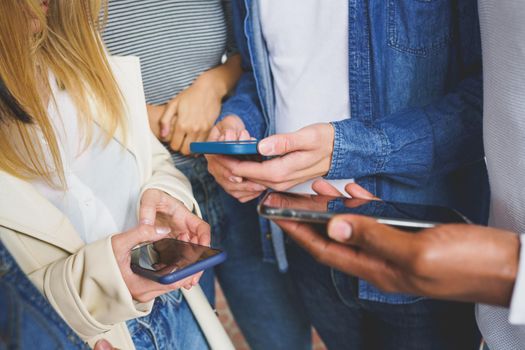 Hands of young unrecognizable people using smartphone outdoors.