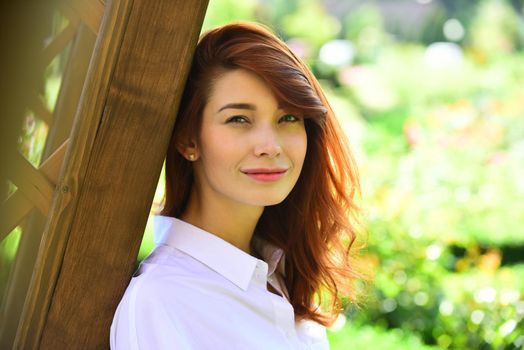 Spring Beautiful romantic red haired girl in white lace dress standing near blooming tree. Woman in the garden