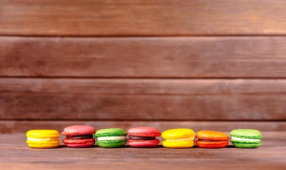 Colorful sweet macarons dessert in a row on wooden table. Copy-space in upper part of image.