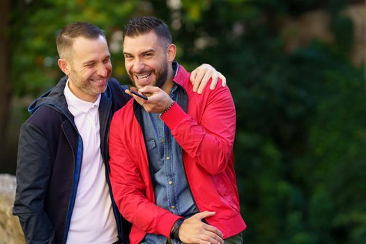 Gay couple recording a voice note together on their smartphone. Homosexual relationship concept.