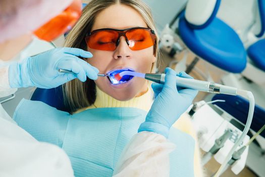 A young beautiful girl in dental glasses treats her teeth at the dentist with ultraviolet light. filling of teeth.