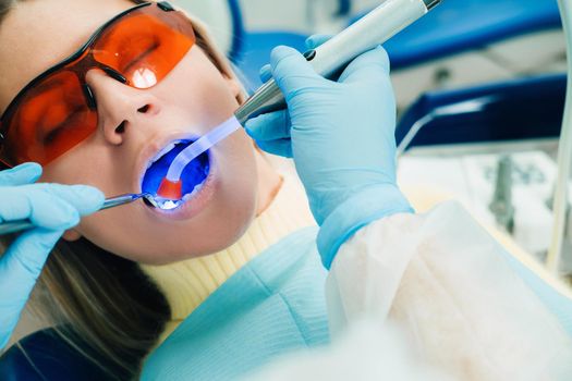 A young beautiful girl in dental glasses treats her teeth at the dentist with ultraviolet light. filling of teeth.