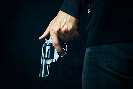 Black revolver with drum in man's hand. Guy with gun down. Firearms for attack or defense. Armed person on dark background.